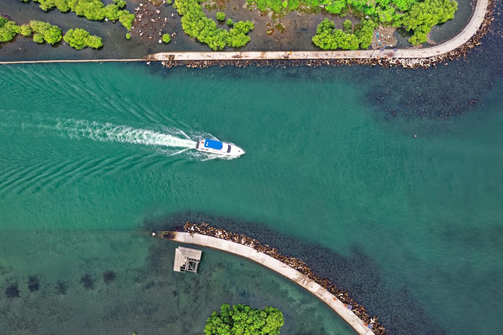 Aerial view of a boat navigating through the vibrant green waters of Penjaringan, Jakarta, Indonesia.