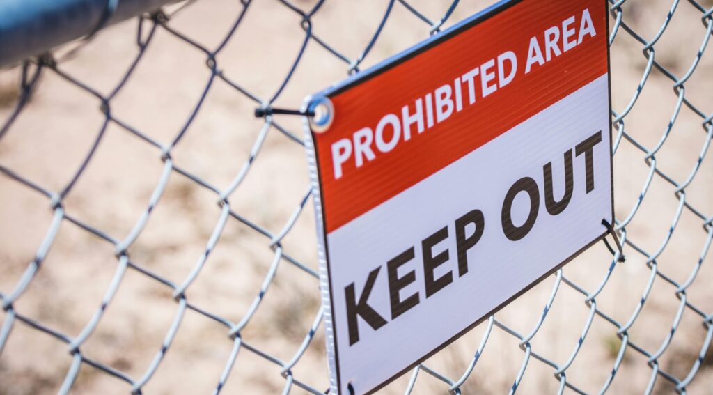 Close-up of a 'Prohibited Area' and 'Keep Out' sign on a chain link fence.